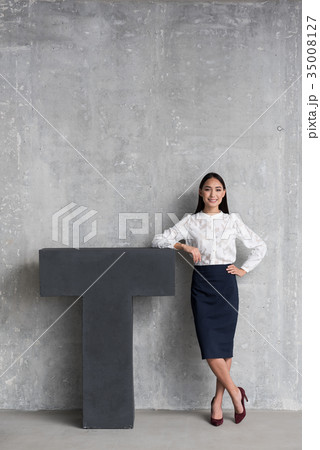 Cheerful businesswoman standing near big T 35008127