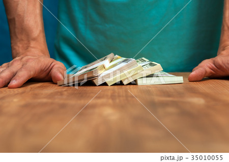 Man standing next to the table with currency heaps Man standing next to the table with currency heaps 35010055