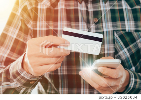 young man holding credit card and use smartphone young man holding credit card and use smartphone 35025034