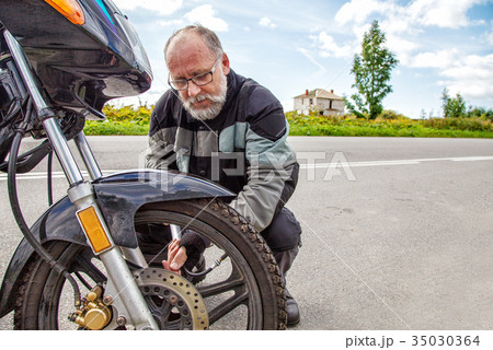 elderly man checks his motorcycle's wheel elderly man checks his motorcycle's wheel 35030364