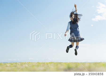 女子高生 海 草原 ジャンプの写真素材
