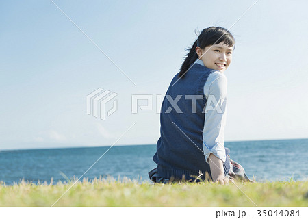 女子高生 海 草原 座る 振り向くの写真素材