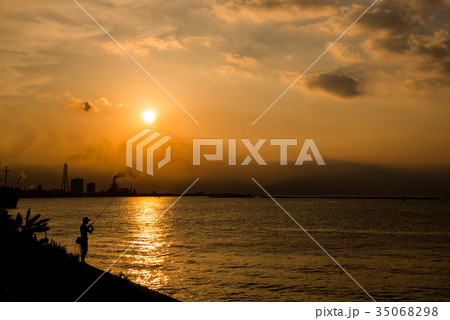 夕日 夕方 夕焼け 海 釣り人 シルエット 海岸線 逆光 海岸線の写真素材