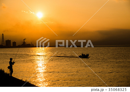 夕日 夕方 夕焼け 海 釣り人 シルエット 海岸線 逆光 海岸線の写真素材