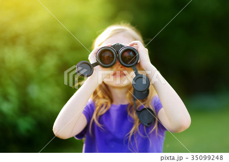 Funny little girl looking through binoculars on sunny summer day Funny little girl looking through binoculars on sunny summer day 35099248