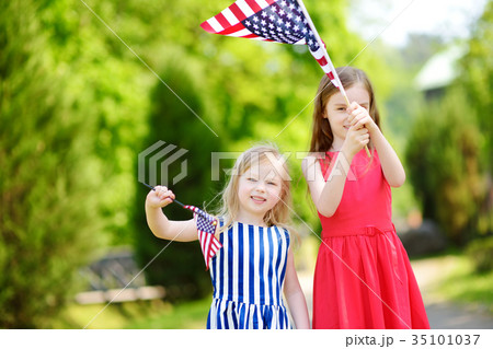 Two adorable little sisters holding american flags outdoors on beautiful summer day. 35101037