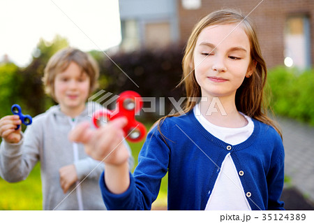 Two funny friends playing with fidget spinners on the playground 35124389