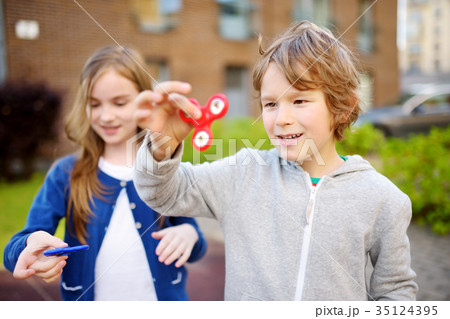 Two funny friends playing with fidget spinners on the playground 35124395