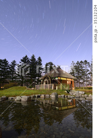 月明かりの夜に茅葺きの水車小屋と池を星の光跡と共に長時間露光で撮影の写真素材