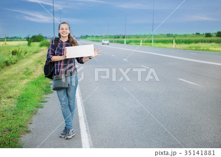 Smiling woman hitchhiker on the road is holding a 35141881