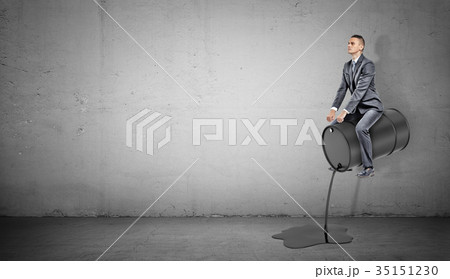A small businessman sits on a black barrel leaking A small businessman sits on a black barrel leaking 35151230