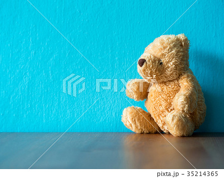 The brown teddy bear sitting on wood table. 35214365