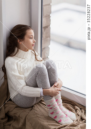 sad girl sitting on sill at home window in winter 35228237