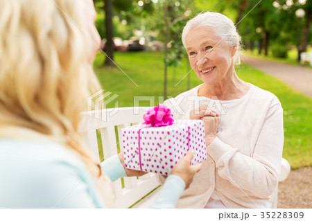 daughter giving present to senior mother at park daughter giving present to senior mother at park 35228309