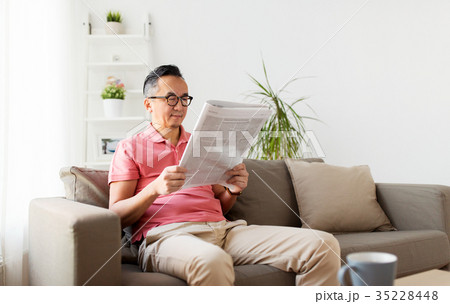 asian man in glasses reading newspaper at home 35228448