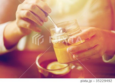 close up of woman adding honey to tea with lemon 35229492