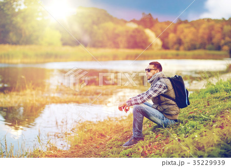 man with backpack resting on river bank 35229939
