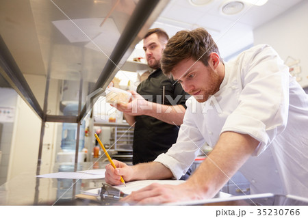 chef and cook with lists or bills at kitchen chef and cook with lists or bills at kitchen 35230766