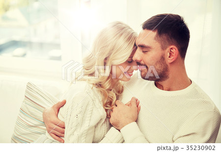 happy couple covered with plaid on sofa at home 35230902