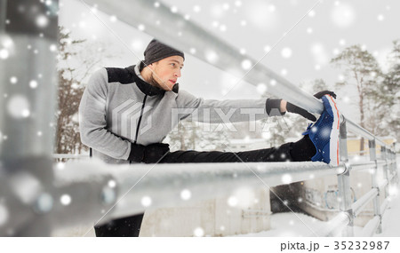sports man stretching leg at fence in winter 35232987