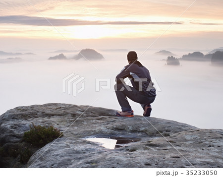 Tourist sit on peak of rock and watching into mist 35233050