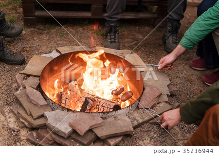 Grilling sausages over a campfire, campers Grilling sausages over a campfire, campers 35236944