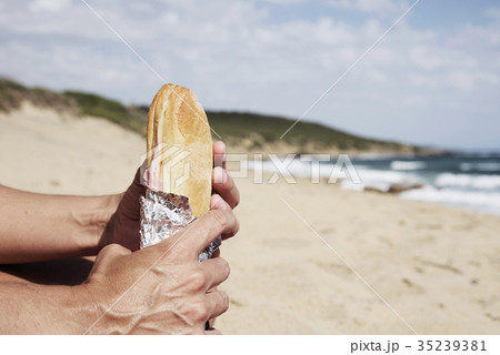 young man eating a sandwich on the beach 35239381