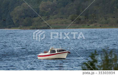 Small boat on the lake, many birds flying over it 35303934