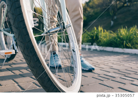 Wheel of a bicycle and female feet in sneakers Wheel of a bicycle and female feet in sneakers 35305057