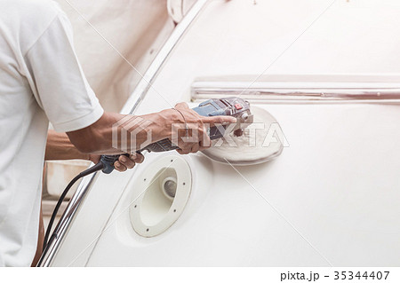 Yacht maintenance. A man polishing side of the white boat in the marina 35344407