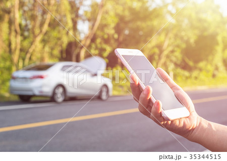 Hand of woman using smartphone and blur of her broken car parking on the road. Contacting car technician or need help concept Hand of woman using smartphone and blur of her broken car parking on the road. Contacting car technician or need help concept 35344515