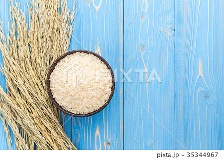 Dried paddy rice crop and jasmine rice in bowl on blue wooden board. With free space for text or design 35344967