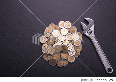 Repair or fixing money or financial concept. Industrial tool and pile of coin on black stone board. Top view for business use Repair or fixing money or financial concept. Industrial tool and pile of coin on black stone board. Top view for business use 35345129
