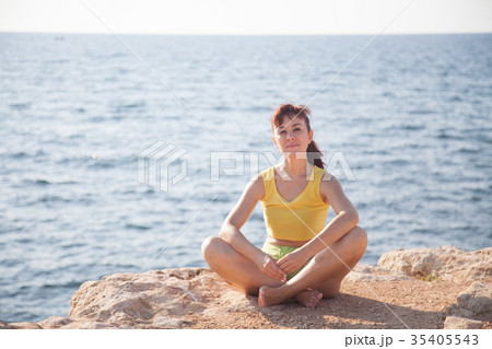 the girl is engaged in yoga sits on the cliff by the girl is engaged in yoga sits on the cliff by 35405543