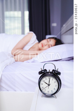 alarm clock on table and woman sleeping on bed in bedroom 35430617