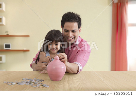 Father and daughter inserting coin in piggy bank Father and daughter inserting coin in piggy bank 35505011