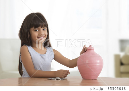 Portrait of little girl inserting coins in clay piggy bank 35505018