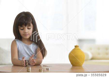 Girl arranging coins on table with clay piggy bank 35505029