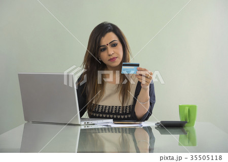 Woman shopping online from mobile phone and credit card sitting at table with laptop Woman shopping online from mobile phone and credit card sitting at table with laptop 35505118