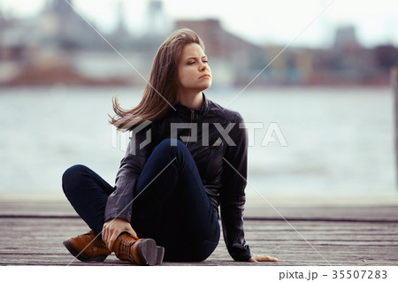 Young adult woman sitting on a wooden jetty on the river Young adult woman sitting on a wooden jetty on the river 35507283