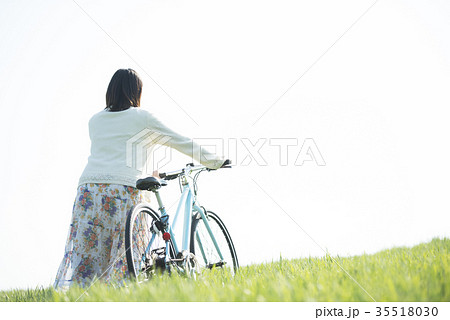 草原で自転車を押す女性の後姿の写真素材