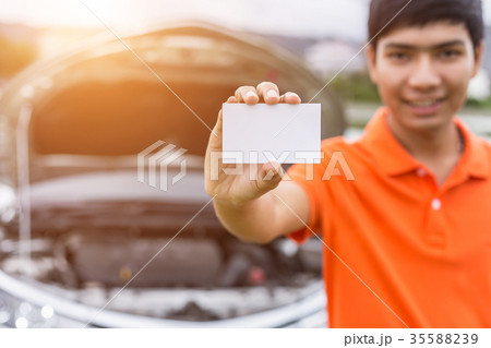 Aian man showing/holding blank of white paper or business card in front of blur damaged car. For car rent or car business 35588239