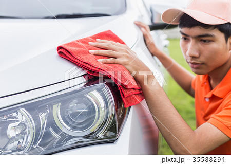 Young man using red microfiber cloth cleaning body of new silver car. For car maintenance concept.. 35588294