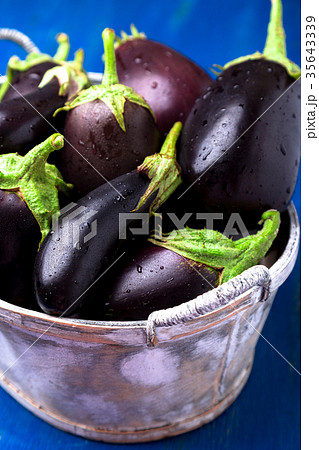 Fresh eggplant in grey basket on blue wooden tabl 35643339