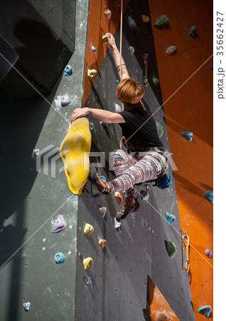 Female climber is climbing up on indoor rock-climbing wall Female climber is climbing up on indoor rock-climbing wall 35662427