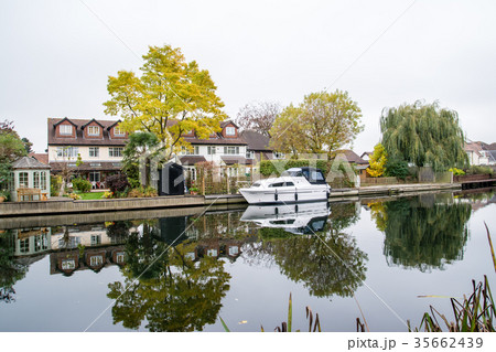 イギリス郊外の田舎にて 川沿いに立つ大きい住宅とすぐ前に停泊するボートの写真素材