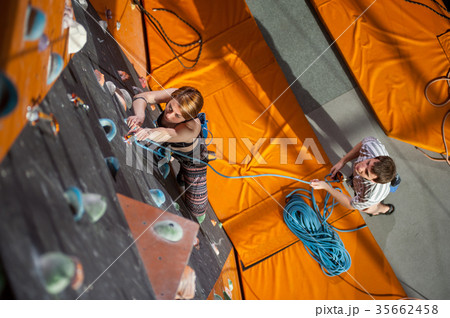 Female climber is climbing up on indoor rock-climbing wall Female climber is climbing up on indoor rock-climbing wall 35662458