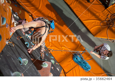 Female climber is climbing up on indoor rock-climbing wall Female climber is climbing up on indoor rock-climbing wall 35662464