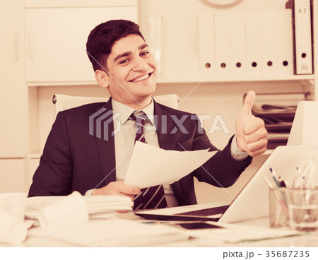 Smiling office manager reading documents about the transaction 35687235