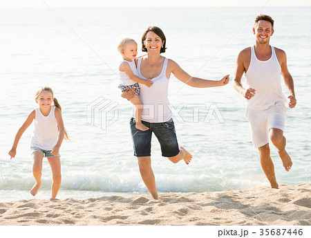 Positive family of four running on sandy beach 35687446
